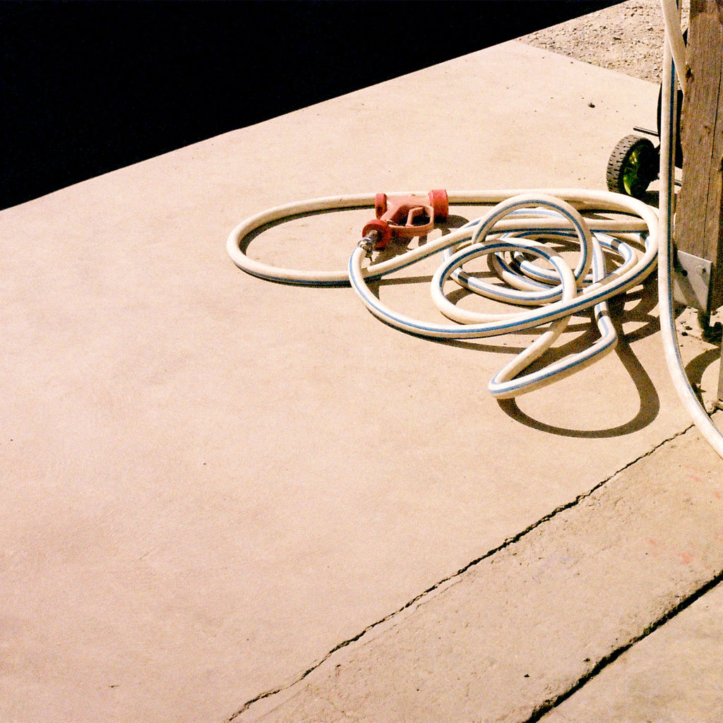 A coiled white washdown hose with a red spray gun handle, resting on a concrete surface outside in the sun.