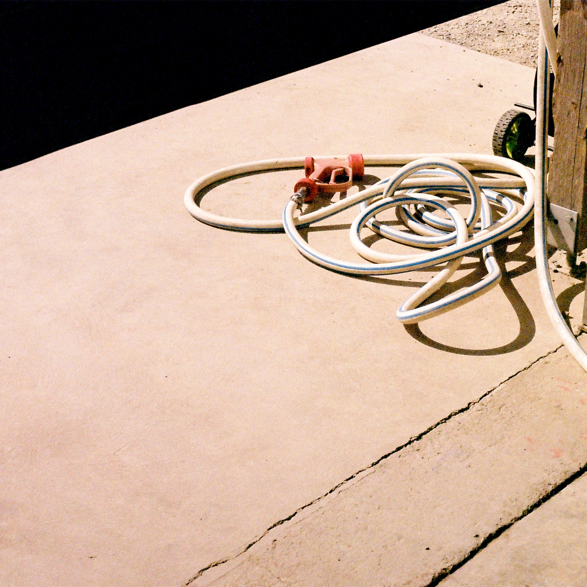 A coiled white washdown hose with a red spray gun handle, resting on a concrete surface outside in the sun.